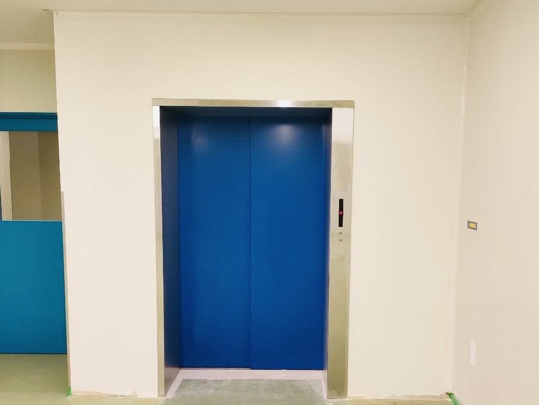 三重県の工場内壁とエレベーター扉のリフレッシュ塗装完了後のアフター写真。鮮やかなブルーの扉と清潔感のある白い壁面。