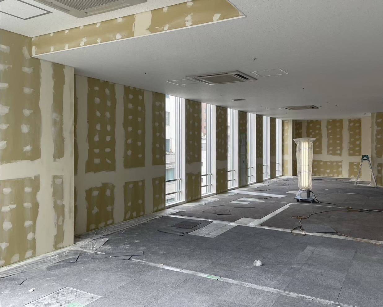 名古屋市のオフィス内装塗装で部屋全体のパテ処理が完了した状態の写真。ボードの継ぎ目やビス穴の下地調整を終えた広いテナント室内。