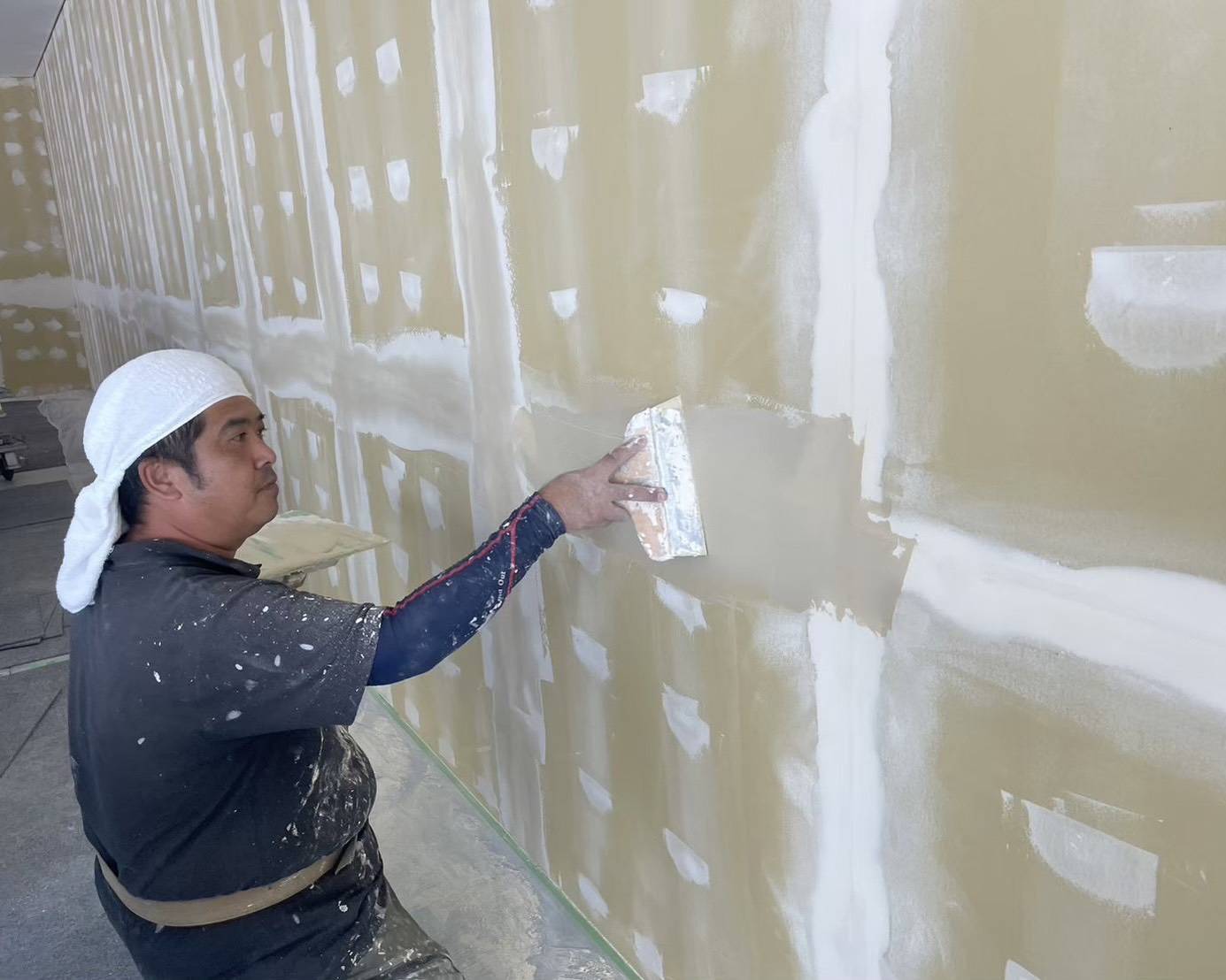 名古屋市のオフィス内装塗装における下地調整・パテ処理の作業風景。ビス頭やボードの継ぎ目を平らに埋める職人の手元写真。