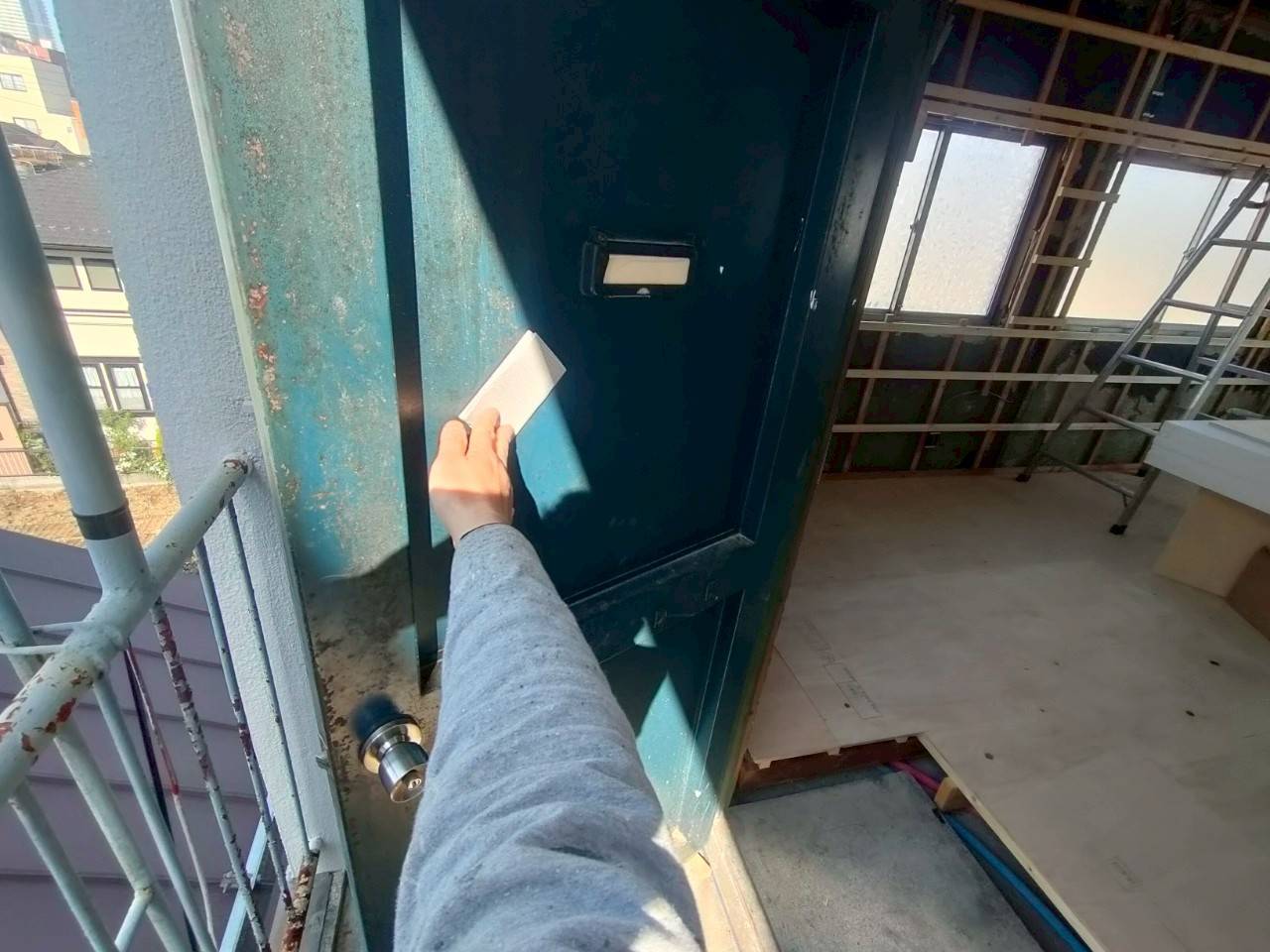 岐阜市のマンション修繕における玄関ドア塗装前の施工前写真。色あせてサビの浮いた鉄扉をケレン処理する職人の手元。
