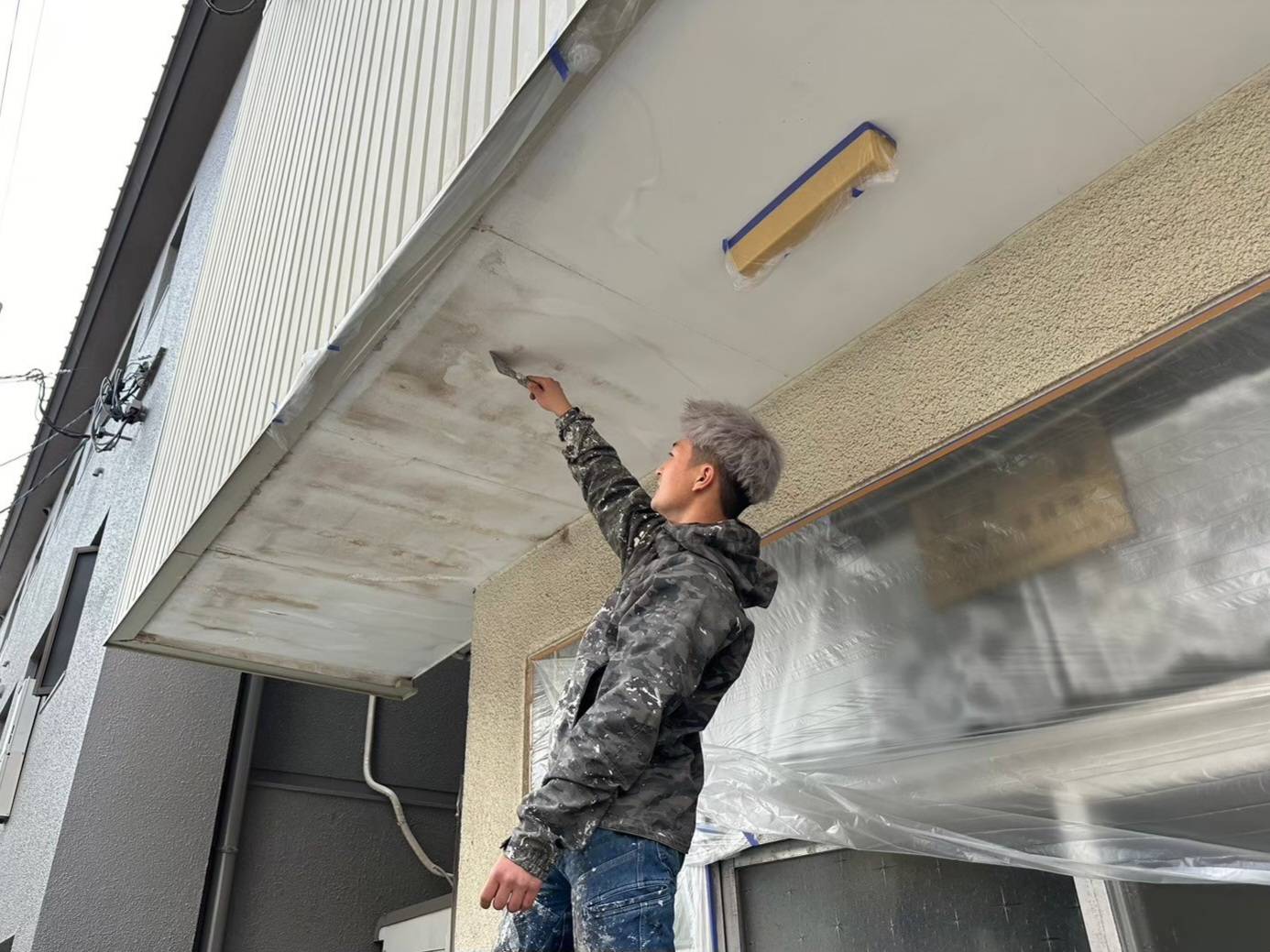 岐阜市のマンション外壁塗装における軒天（天井）のケレン作業・下地調整風景。剥がれかかった古い塗膜をヘラで削り落とす職人の写真。