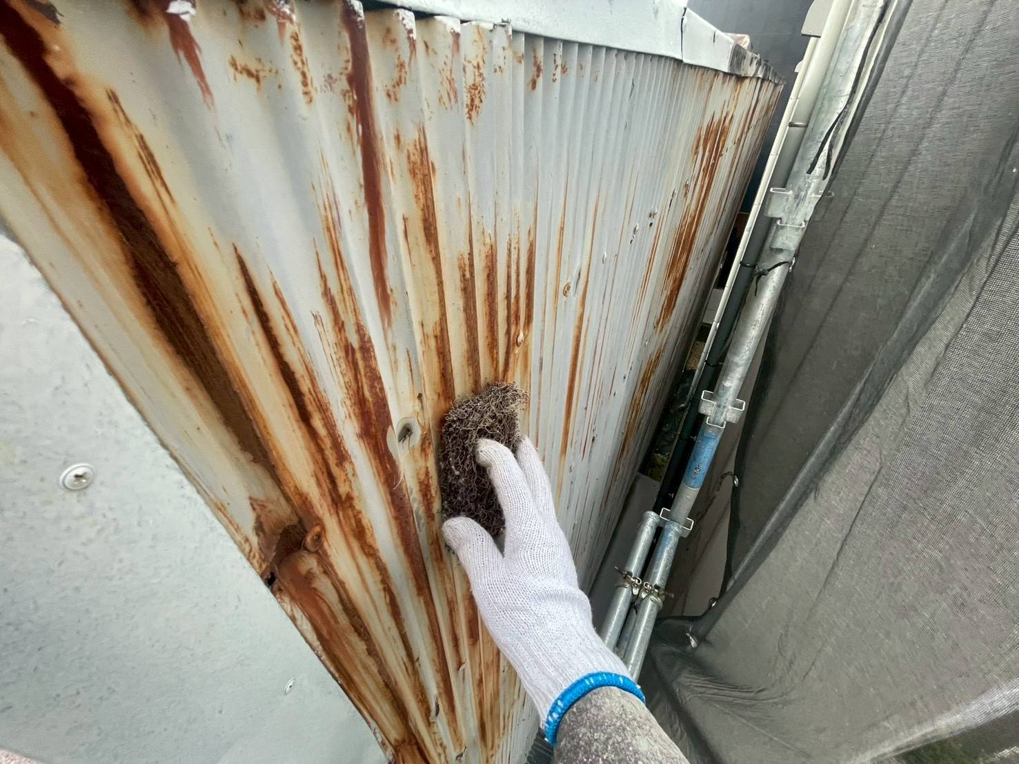 名古屋市西区の店舗塗装におけるトタン外壁のケレン作業。激しい茶サビをマジックロンで削り落とす鉄部下地調整。
